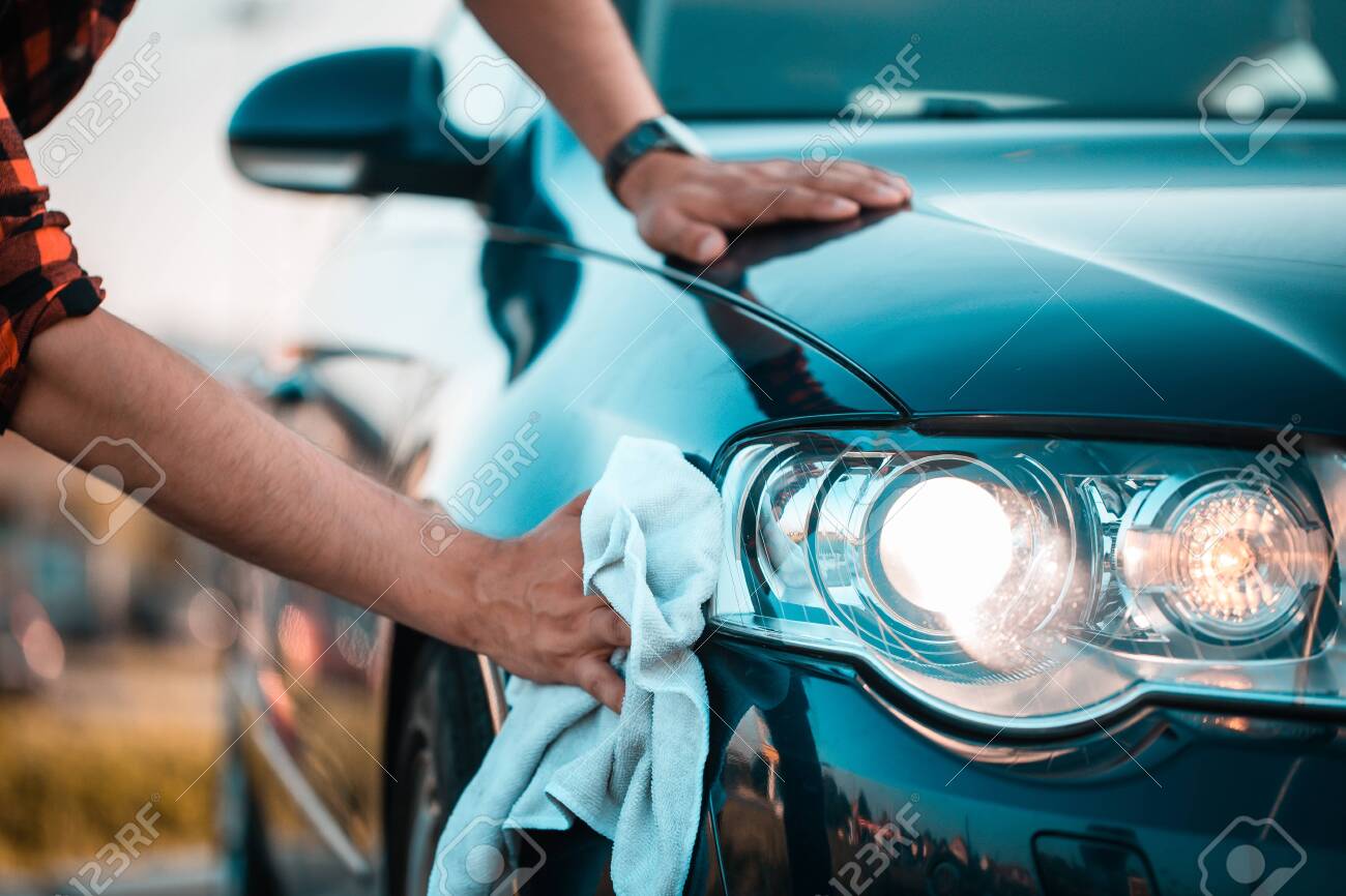 Close up, shoot of a male hands carefully polishing his car with a microfiber cloth, outdoors.